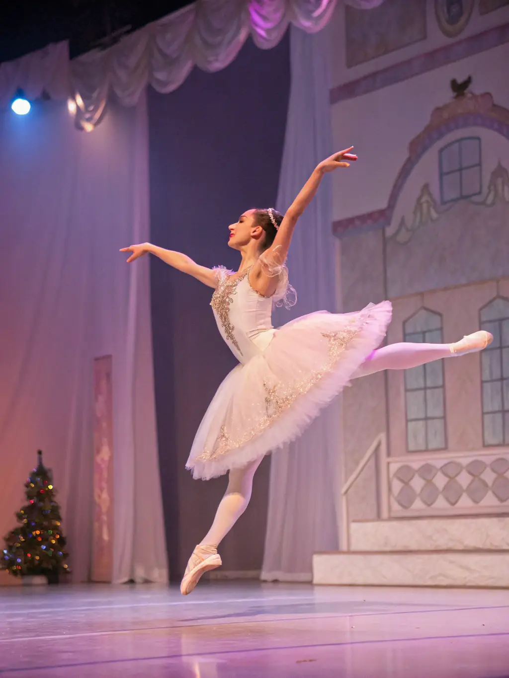 A young ballerina in a graceful pose, wearing a tutu and pointe shoes, performing on a brightly lit stage during a ballet class at Shine Arts Studio Inc.